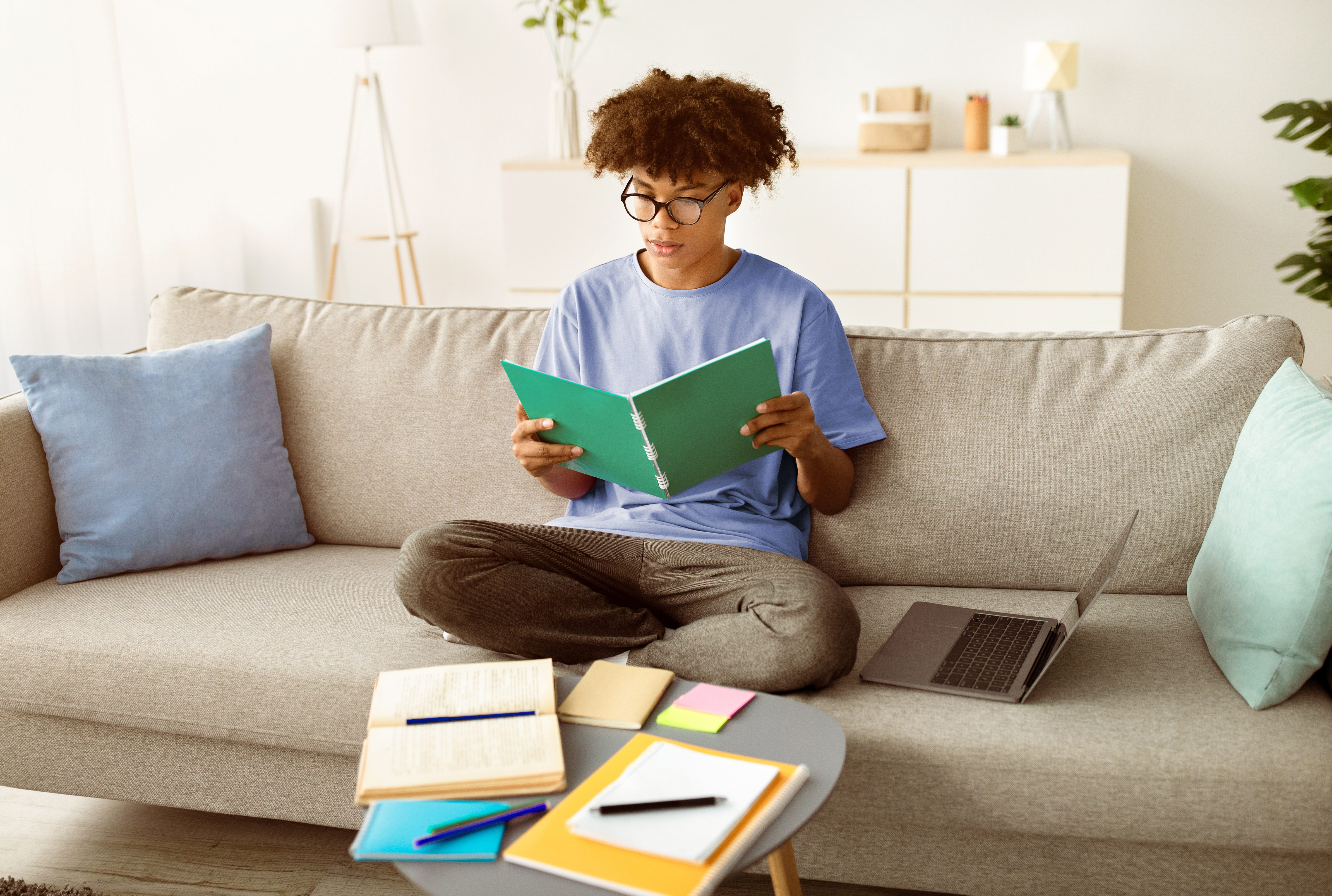 Teenager studying at home, surrounded by textbooks and a laptop, demonstrating the independent learning environment fostered by homeschooling for secondary students.