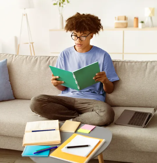Teenager studying at home, surrounded by textbooks and a laptop, demonstrating the independent learning environment fostered by homeschooling for secondary students.
