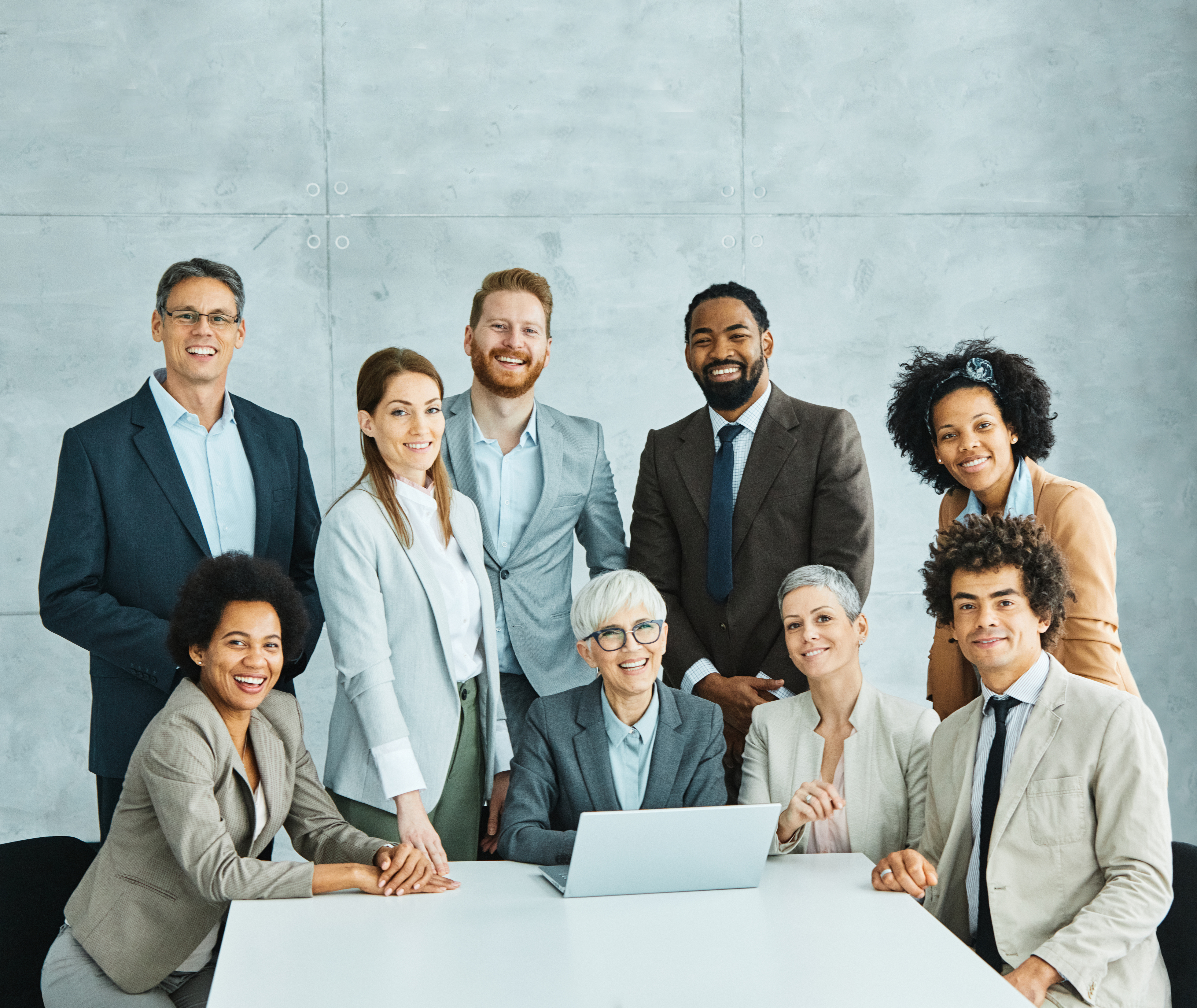 Group of colleagues gathered at a white table, smiling with a laptop in front of them.