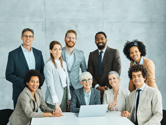 Group of colleagues gathered at a white table, smiling with a laptop in front of them.