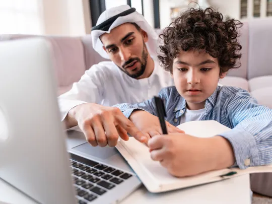 Parental involvement in Jeddah homeschooling: a man guides a young boy through his lessons at home.