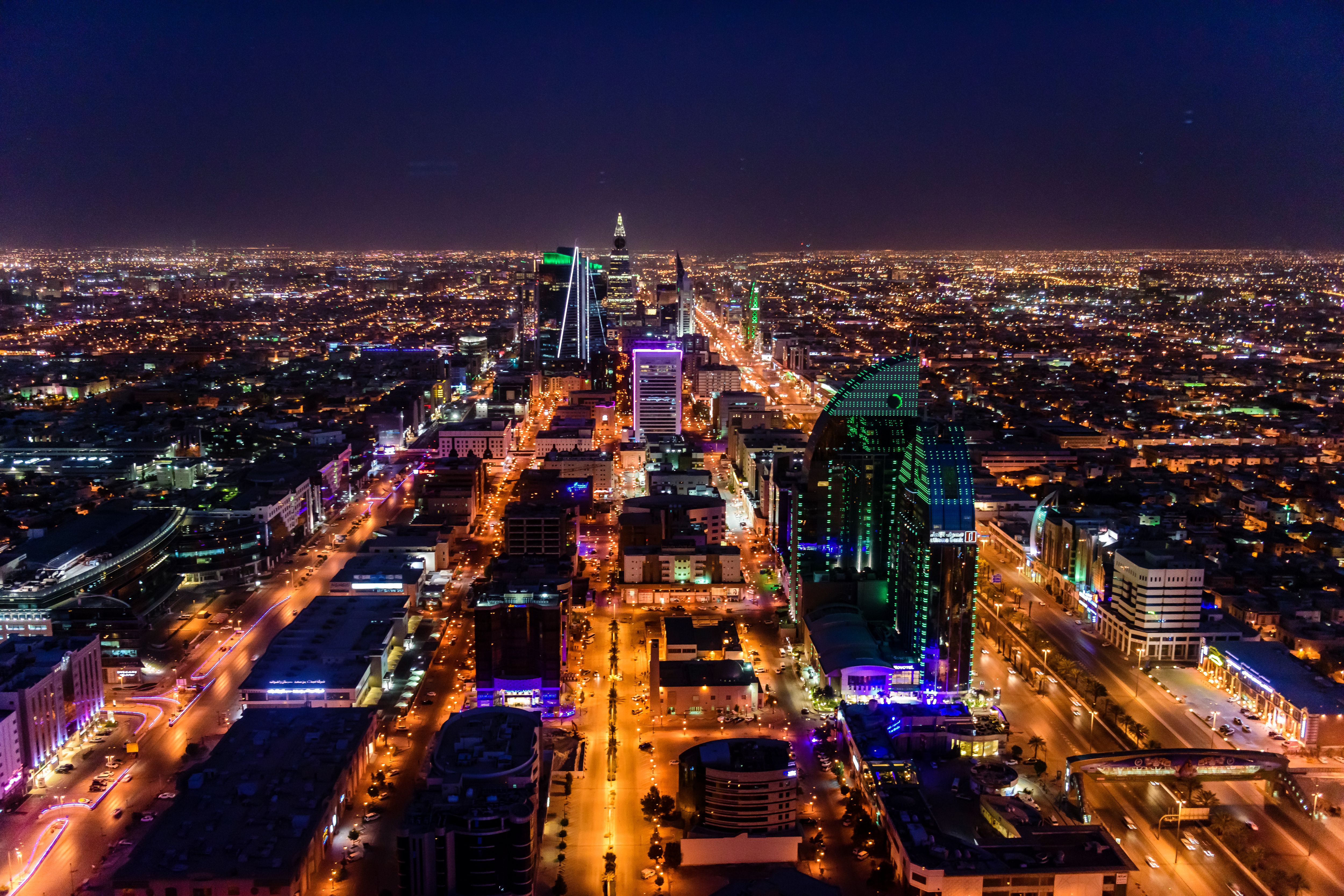 Night view of Riyadh with brightly lit skyscrapers and busy roads stretching into the distance.