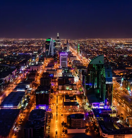 Night view of Riyadh with brightly lit skyscrapers and busy roads stretching into the distance.