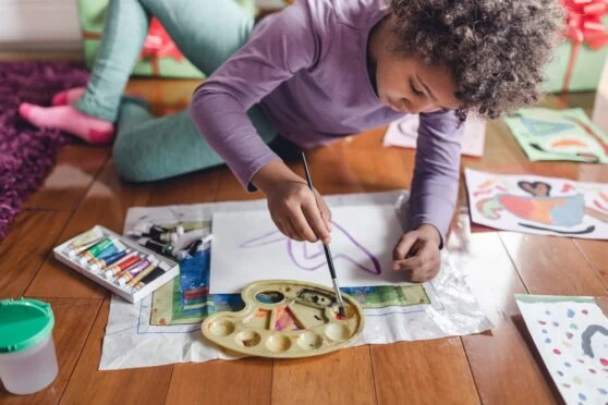A homeschooling young child sitting on the floor and painting a picture. 