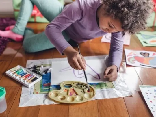 A homeschooling young child sitting on the floor and painting a picture.