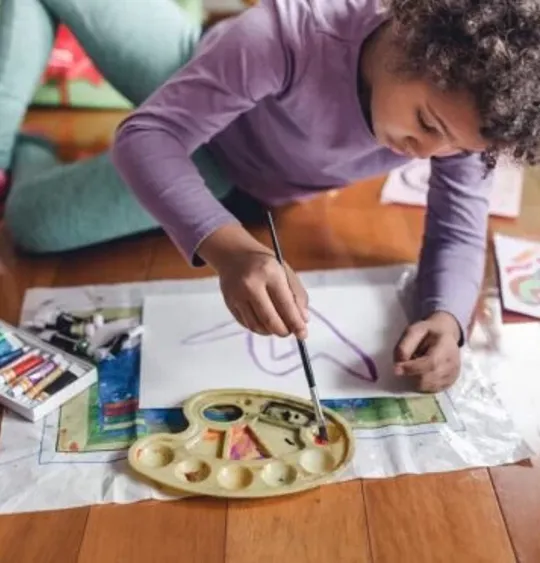 A homeschooling young child sitting on the floor and painting a picture.